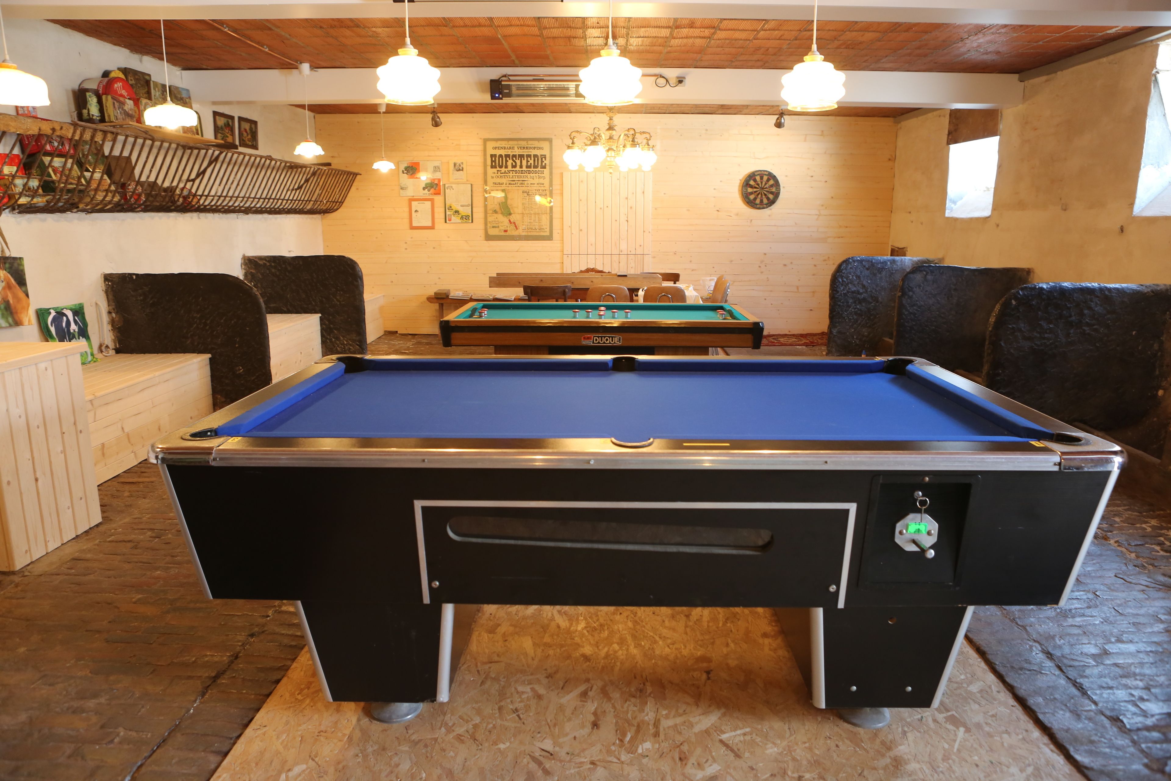 Une table de billard dans une pièce aux murs en bois, un jeu de fléchettes et une étagère contenant divers objets.