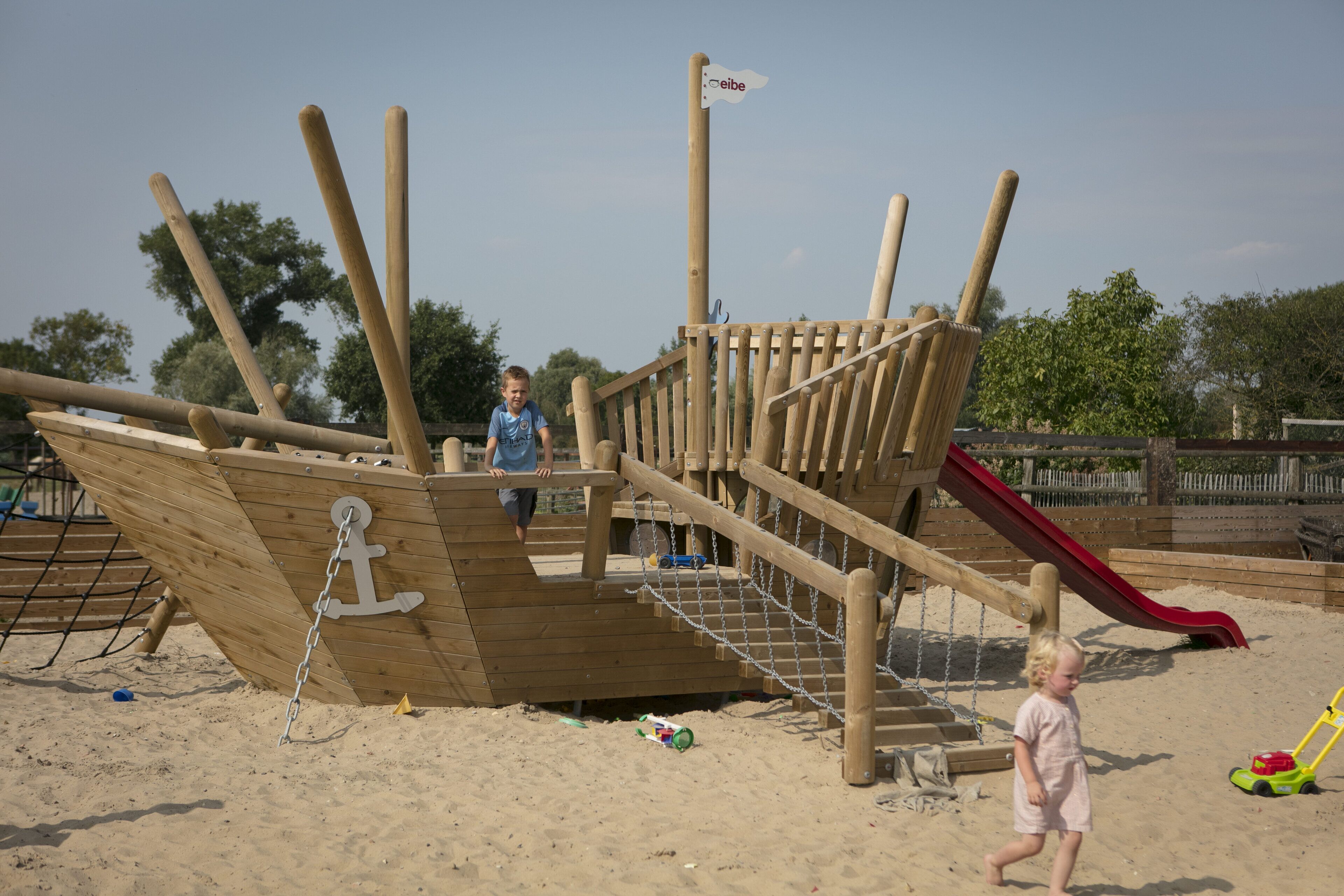 A wooden play structure with a slide and climbing steps.
