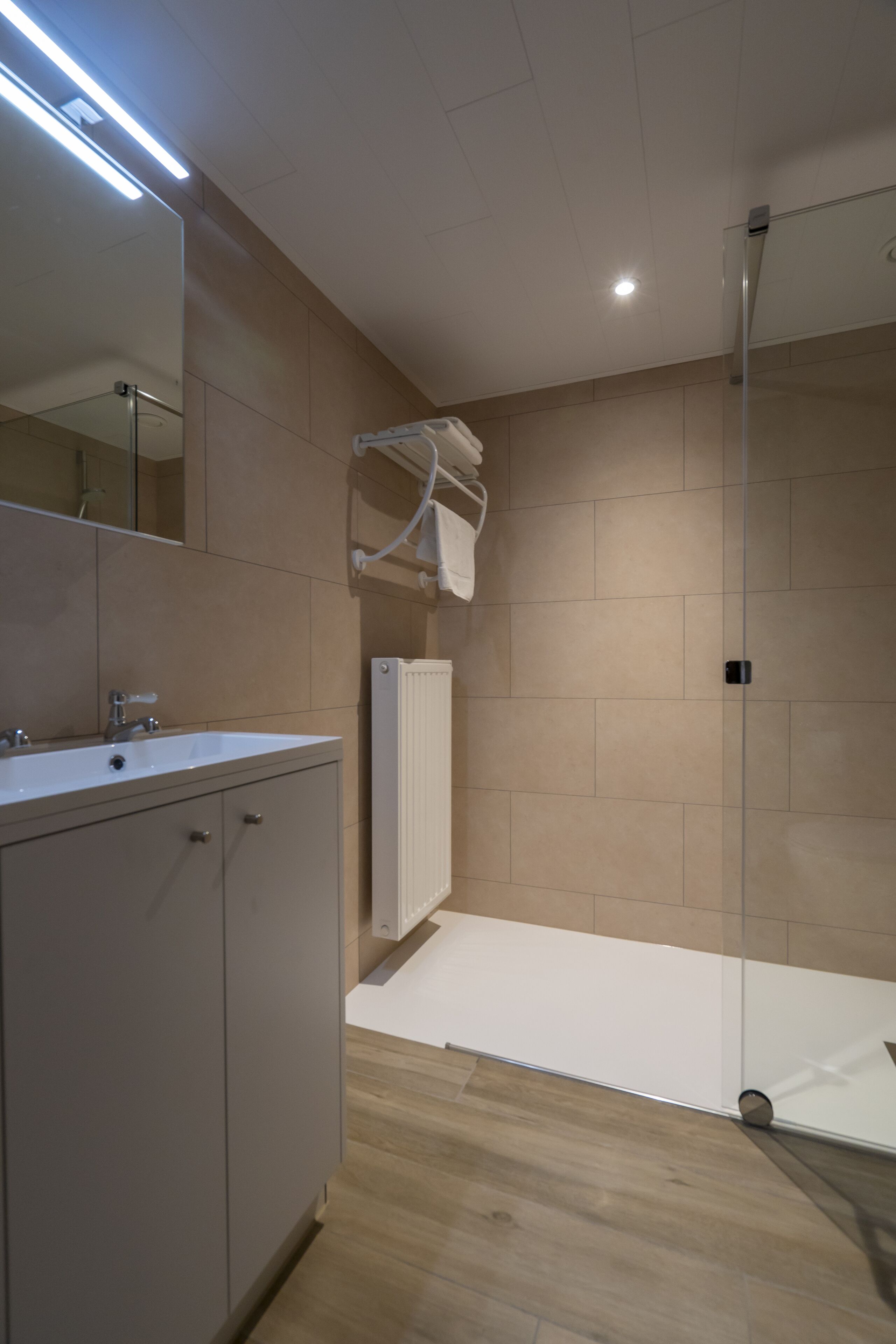 Un baño moderno con un espejo grande, un lavamanos, una ducha y un perchero para toallas.