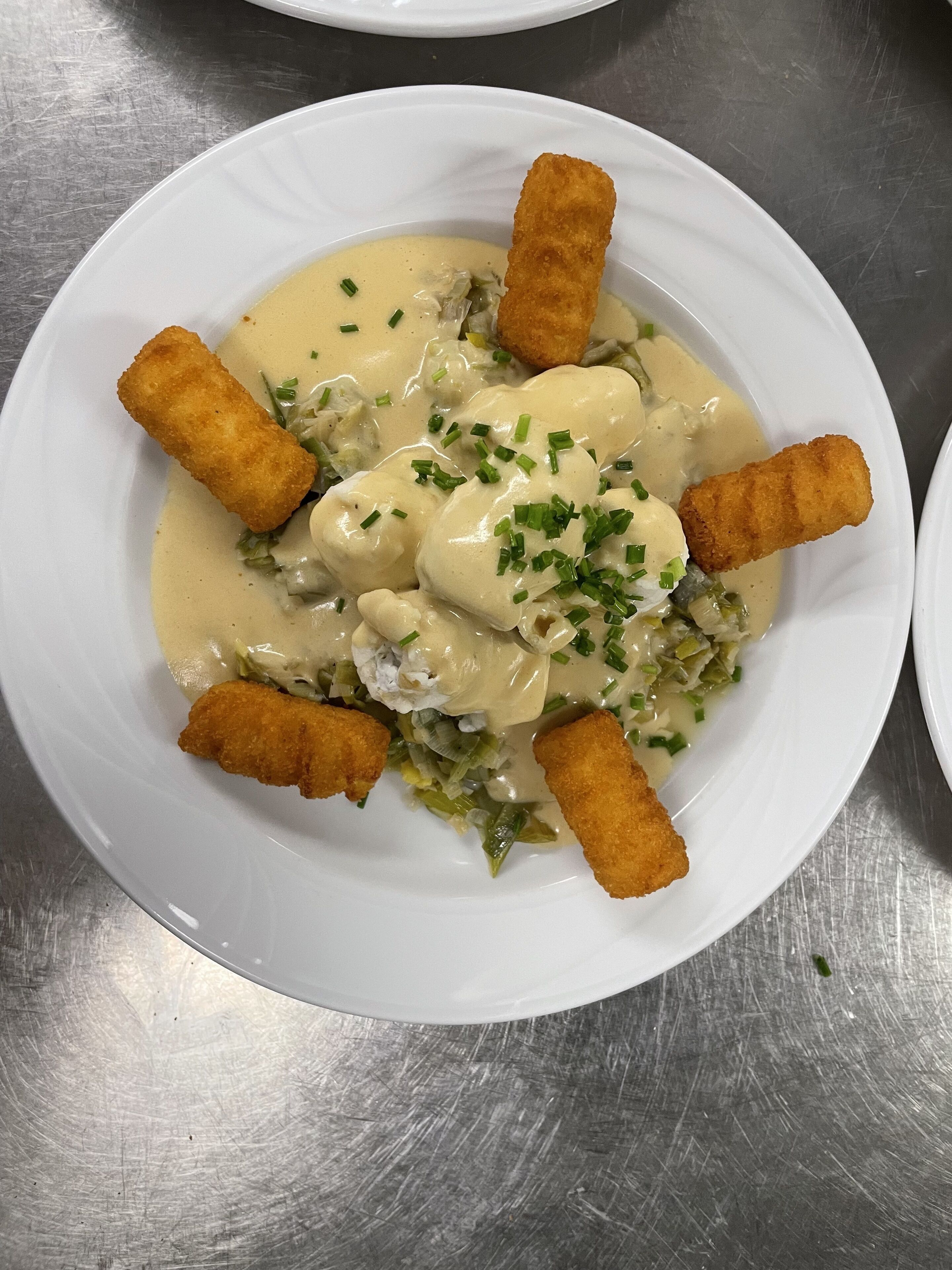Een wit bord met een romige saus, groene groenten en diverse gepaneerde ingrediënten.