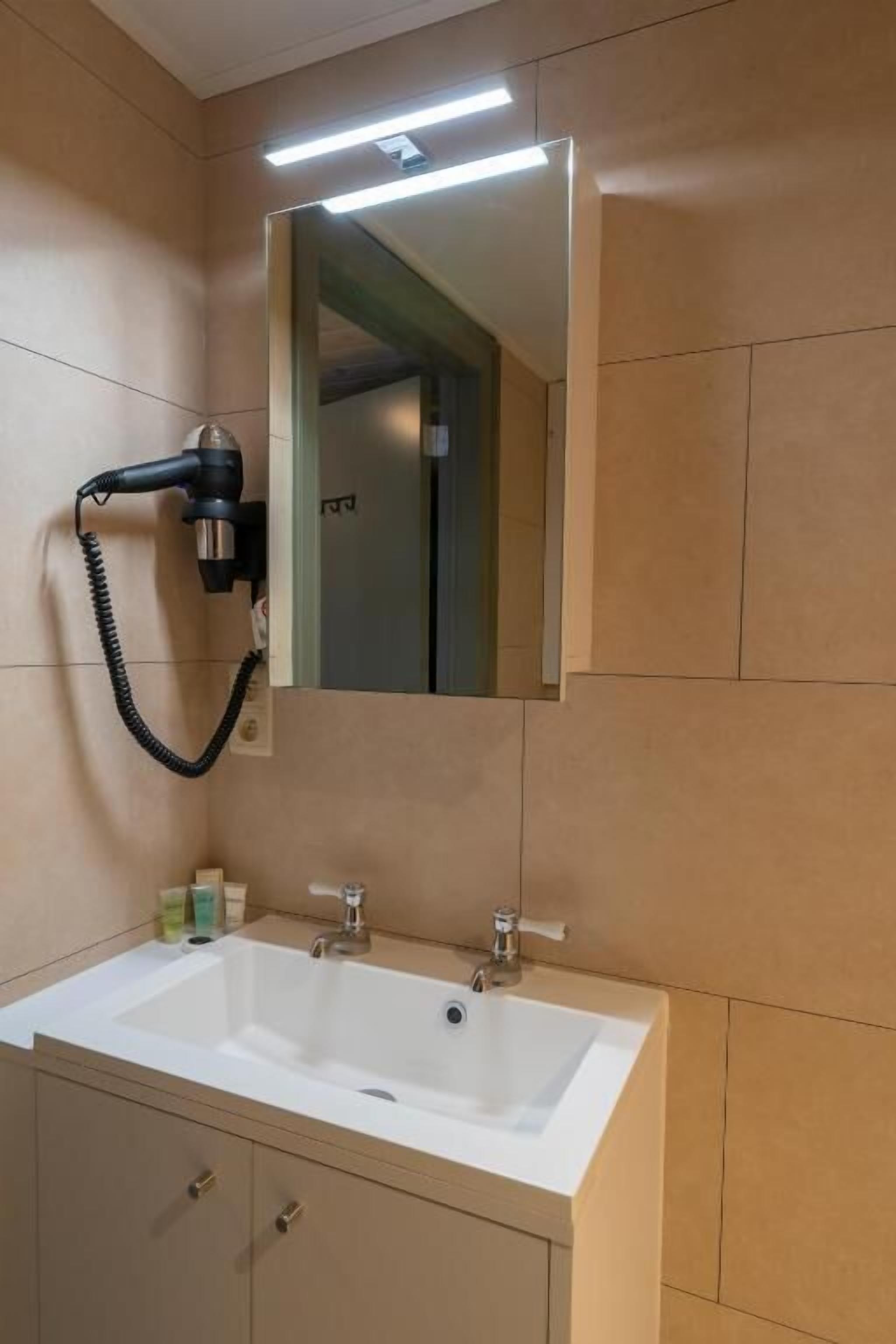 Un baño con un lavabo blanco, un espejo y un secador de pelo fijado a la pared.