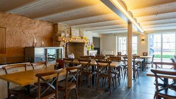 A restaurant with wooden tables and chairs, a brick fireplace, and large windows.