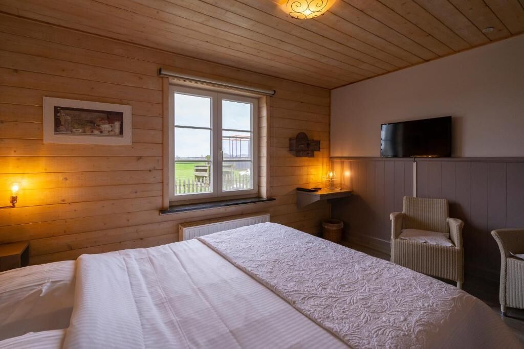 A bedroom with a large bed, wooden walls, a window with a view, a television, and a chair.