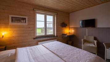 A bedroom with a large bed, wooden walls, a window with a view, a television, and a chair.