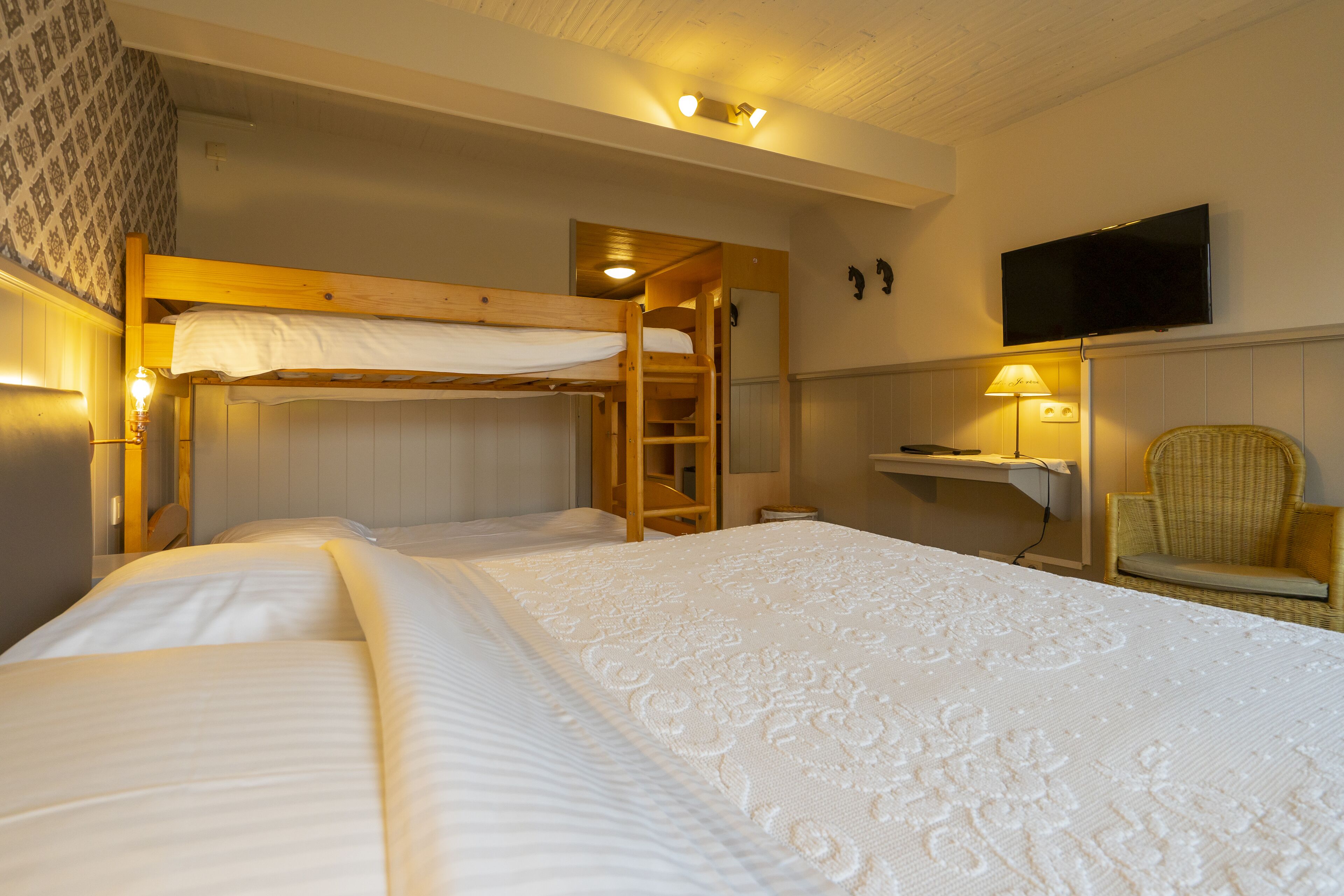 A hotel room with bunk beds, a television, a chair, and a lamp.