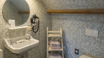 Un baño moderno con una pared de mosaicos, un espejo redondo, un lavabo blanco, un perchero y un inodoro.