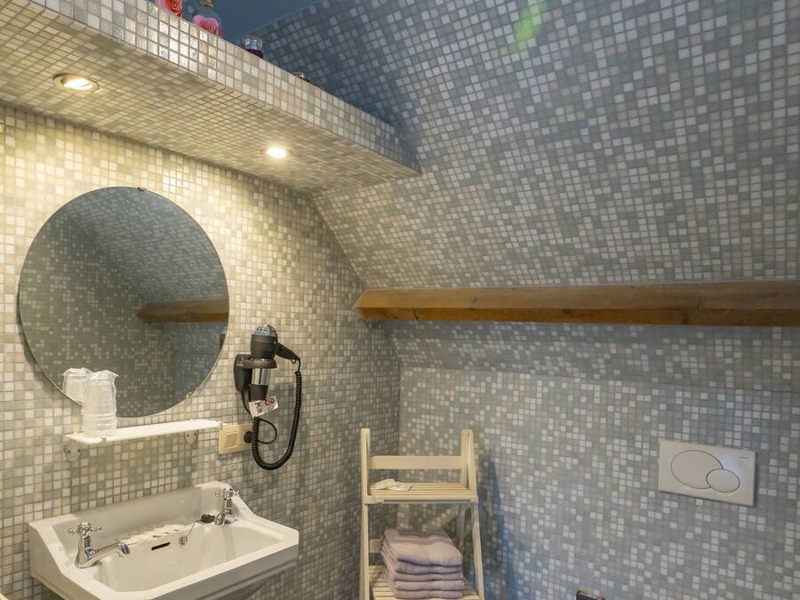 Un baño moderno con una pared de mosaicos, un espejo redondo, un lavabo blanco, un perchero y un inodoro.