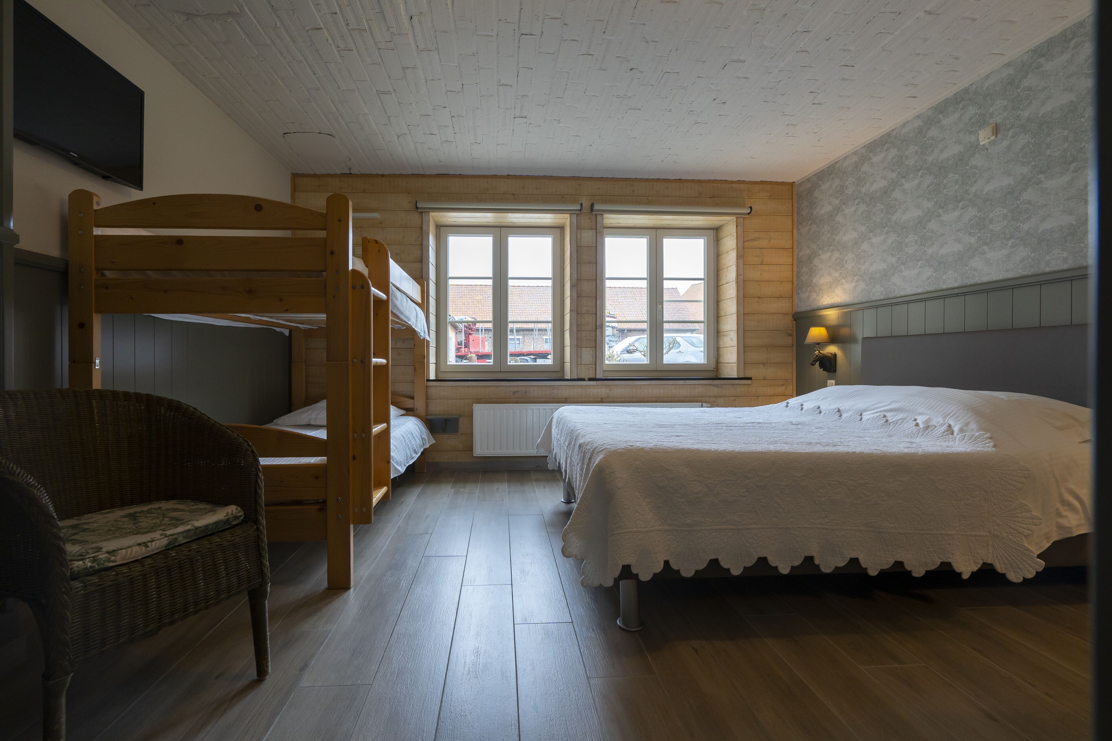Een kamer met een stapelbed, een enkele bed, een rieten stoel, een raam met uitzicht en een aan de muur bevestigde flatscreen televisie.