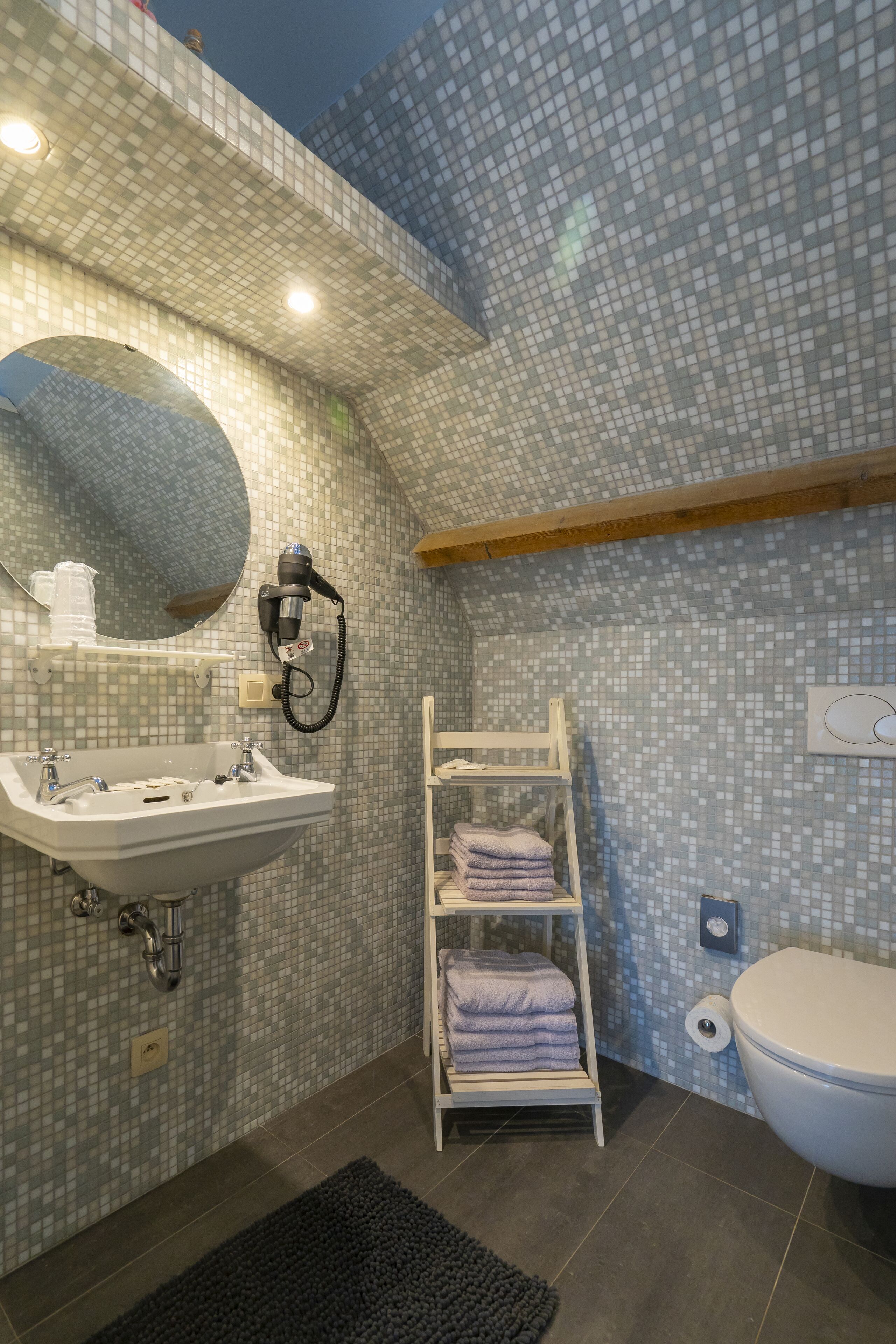 Un baño con pared de mosaicos, un lavamanos, un espejo, un perchero para toallas y un inodoro.