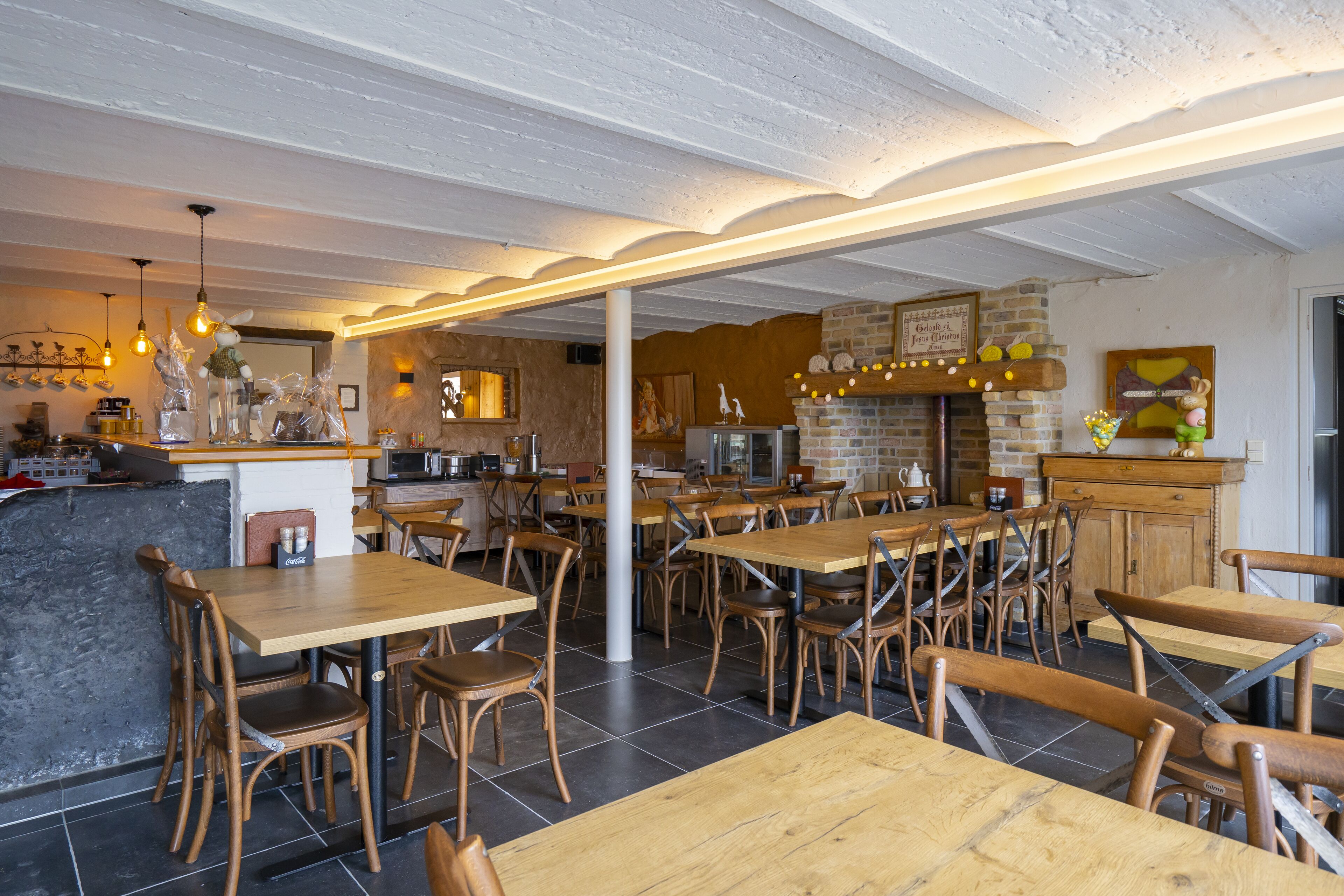 A restaurant with wooden tables and chairs, a brick fireplace, and hanging light fixtures.