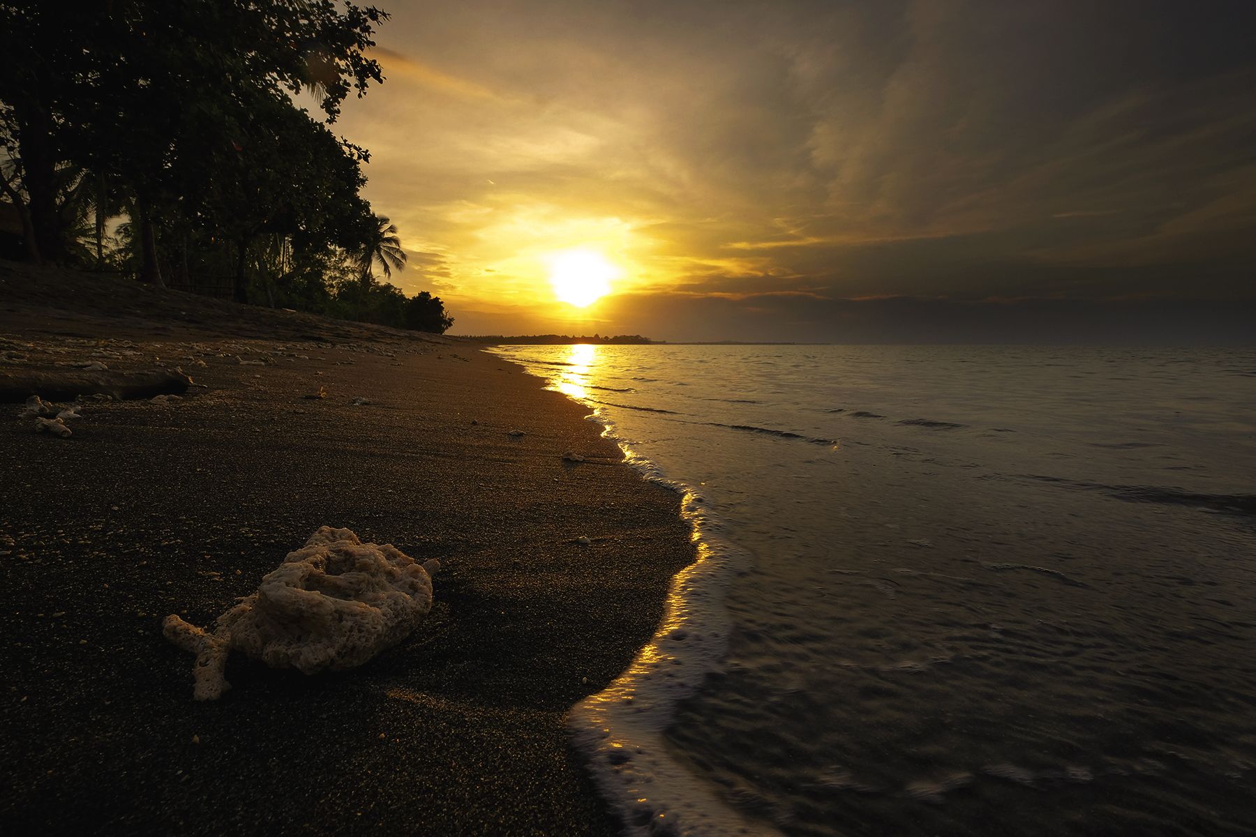 A beach with a sunset, calm sea, and a sandy shore.