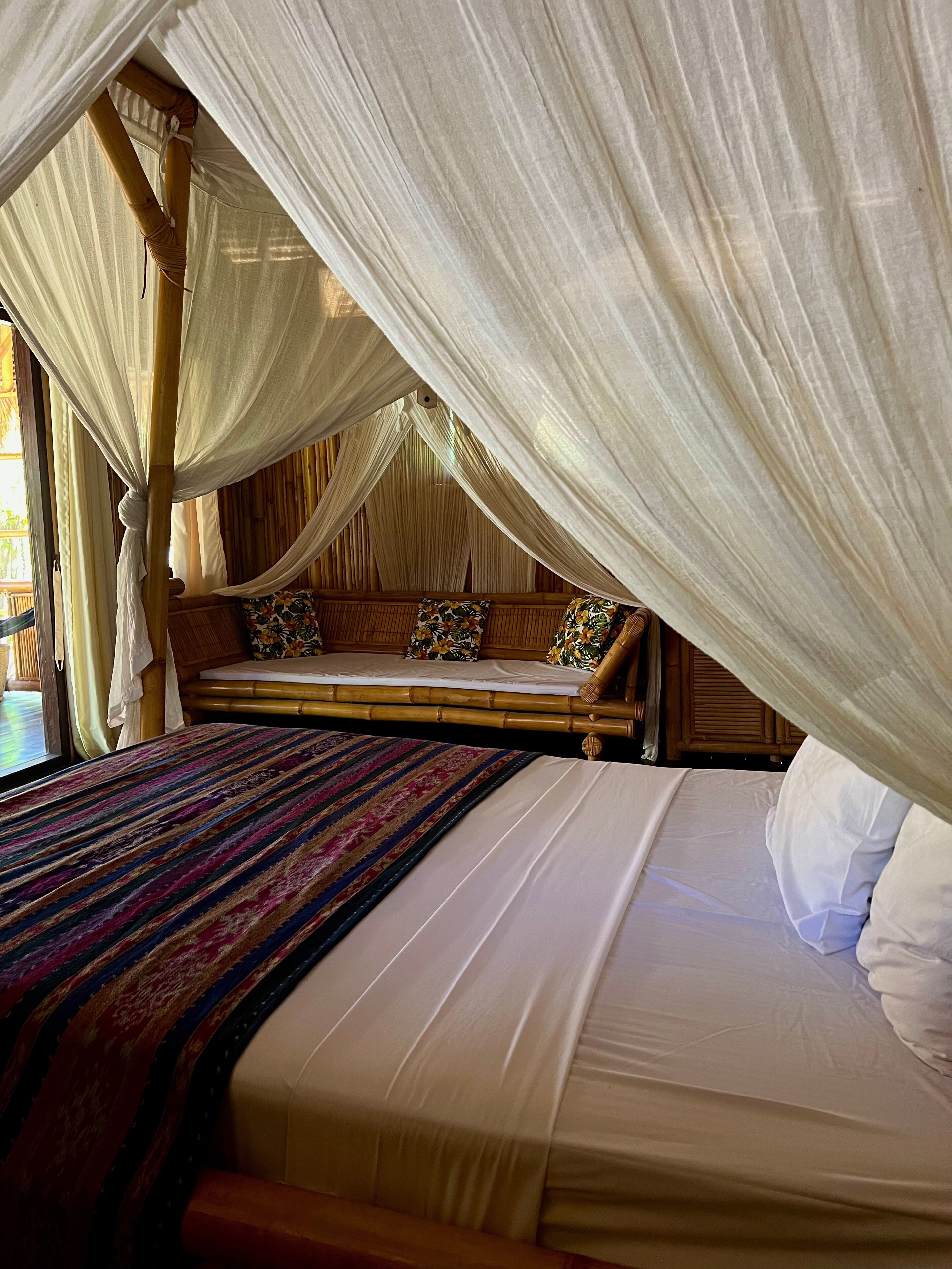 A bed with a canopy, a bench with cushions, and a view of the outdoors.