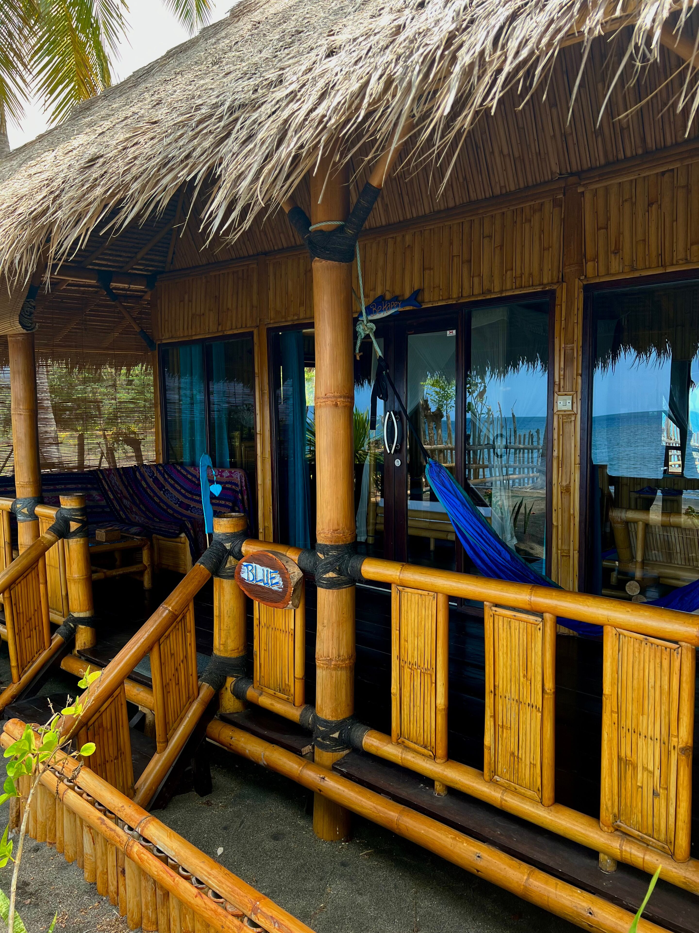 A wooden structure with a thatched roof, bamboo railings, and large windows overlooking the sea.