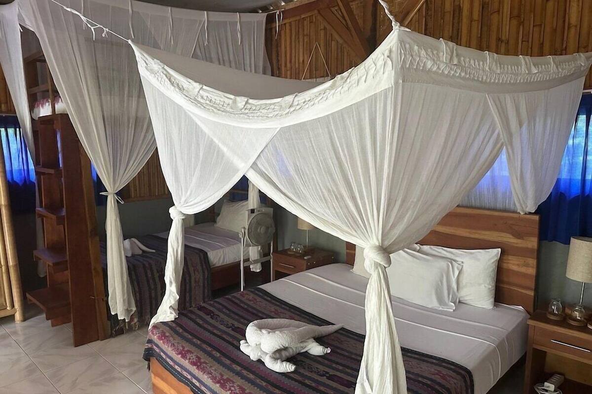 Ein Zimmer mit einem Himmelsbett, einem Nachttisch mit Lampe und einem kleinen Ventilator.