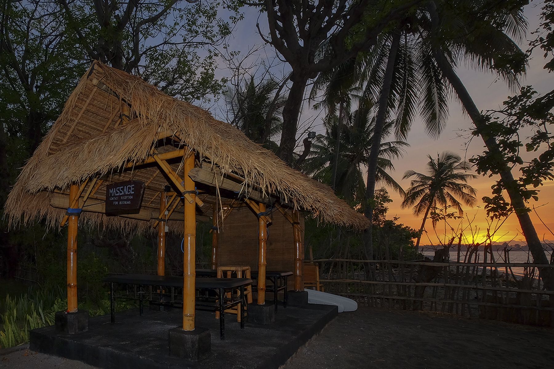 A thatched-roof structure with a sign indicating a massage reception for booking.