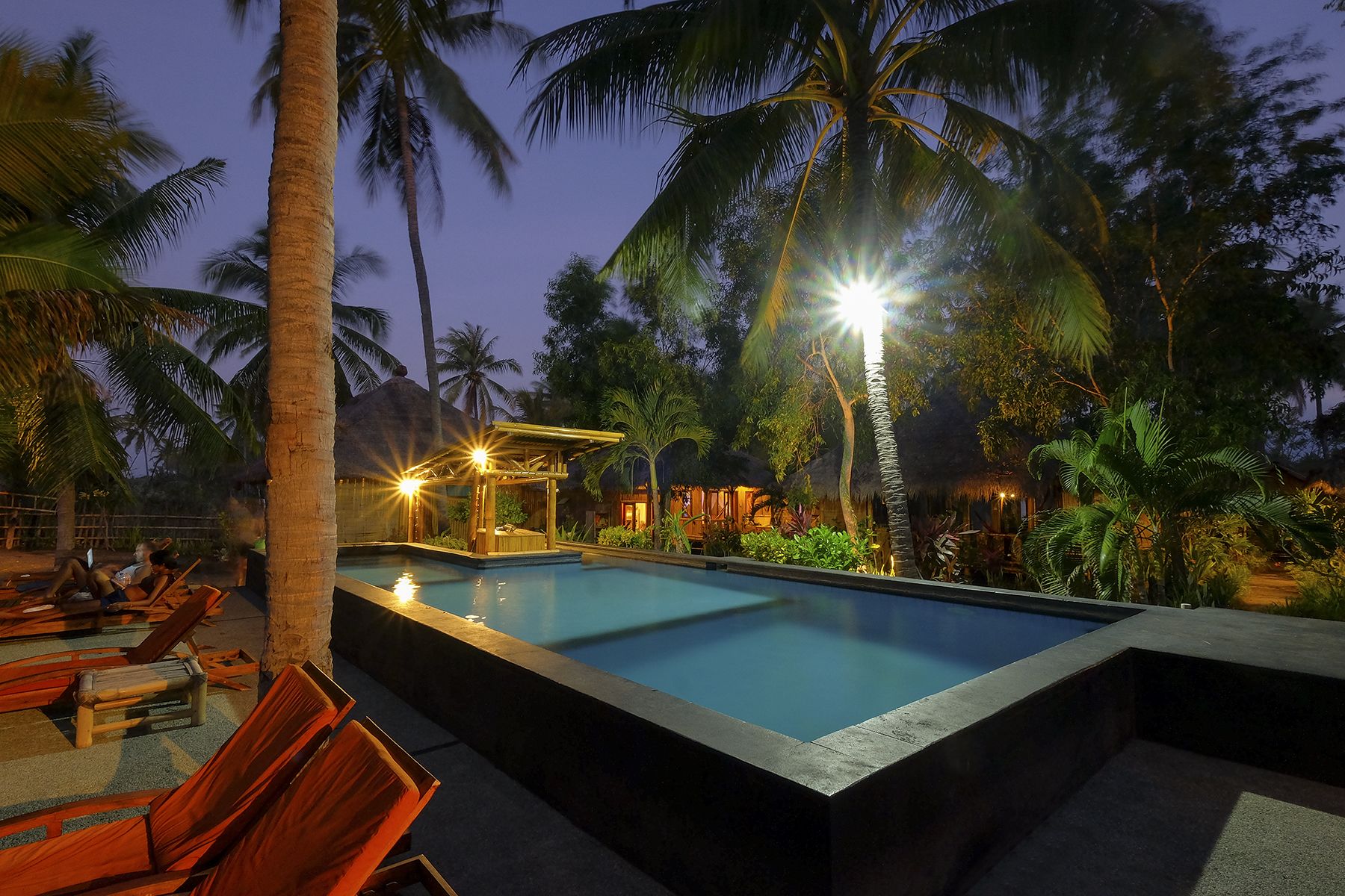 A pool area with lounge chairs and a thatched-roof structure.