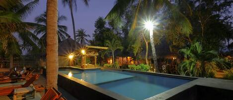 A pool area with lounge chairs and a thatched-roof structure.