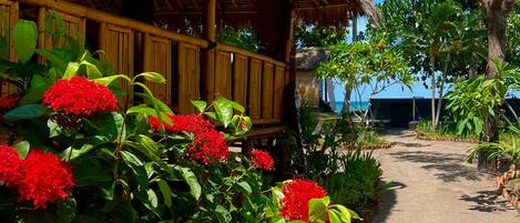 A pathway leading to a thatched-roof building surrounded by lush greenery and red flowers.
