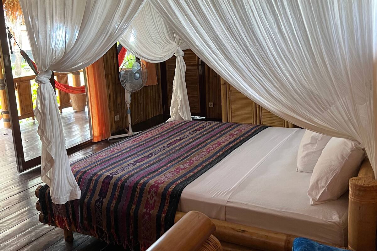 Ein Zimmer mit einem Bett unter einem weißen Baldachin, einem Holz-Kopfteil und einem kleinen Tisch mit weichen Spielsachen.
