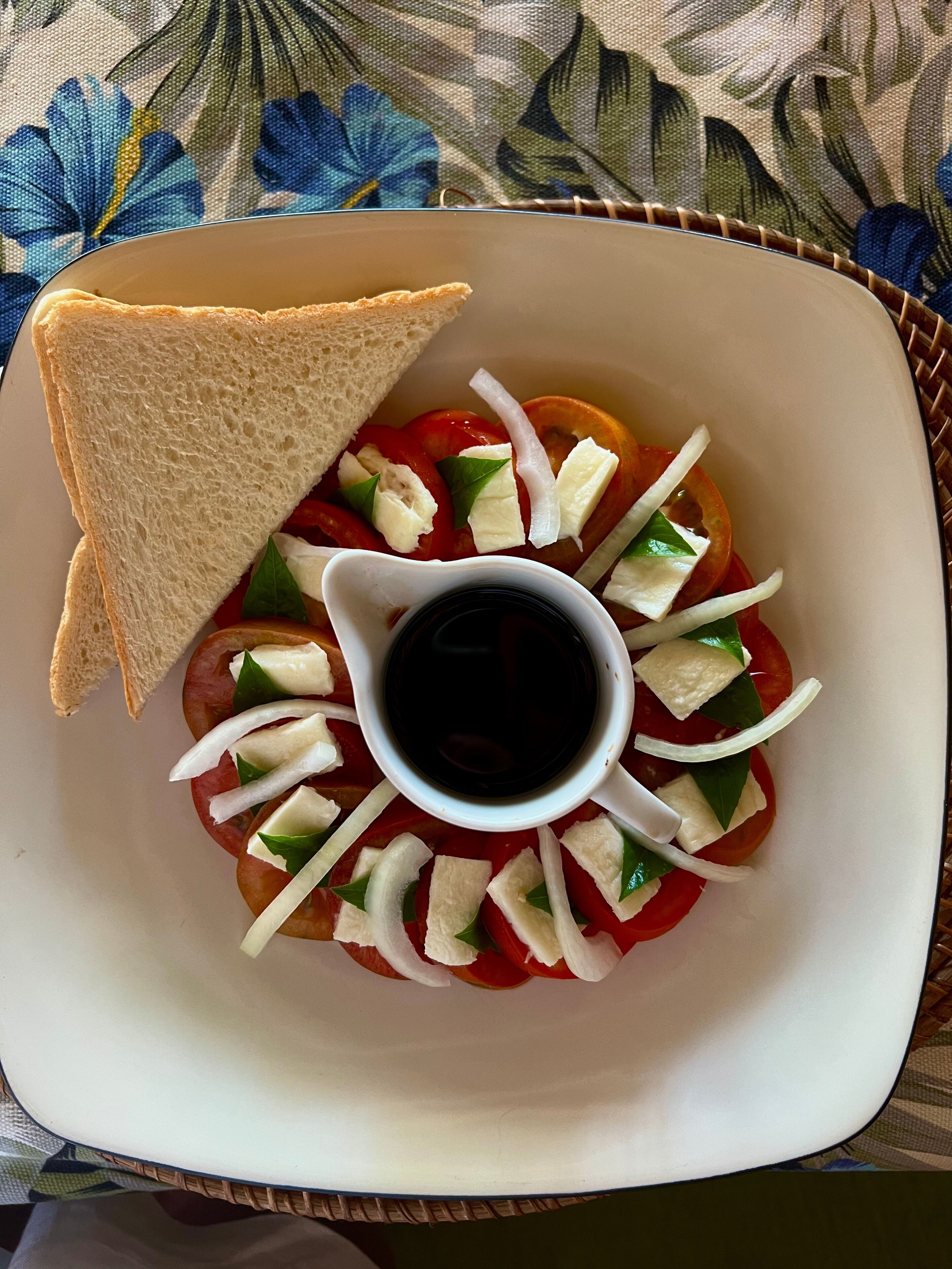 Une assiette avec une salade de tomates, du fromage et une petite coupelle de vinaigrette.