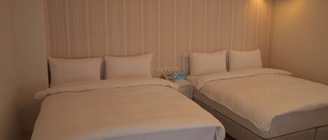 A hotel room with two single beds, a bedside table with a phone, and a wall-mounted light fixture.