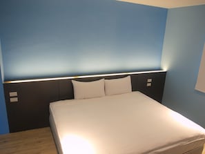 A neatly made bed in a room with blue walls and a modern headboard with built-in lighting. - Taimali Hotel (Taimali)