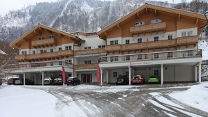 Un hotel de varios pisos con el nombre de un complejo de esquí, una zona de estacionamiento techada y una montaña nevada al fondo.