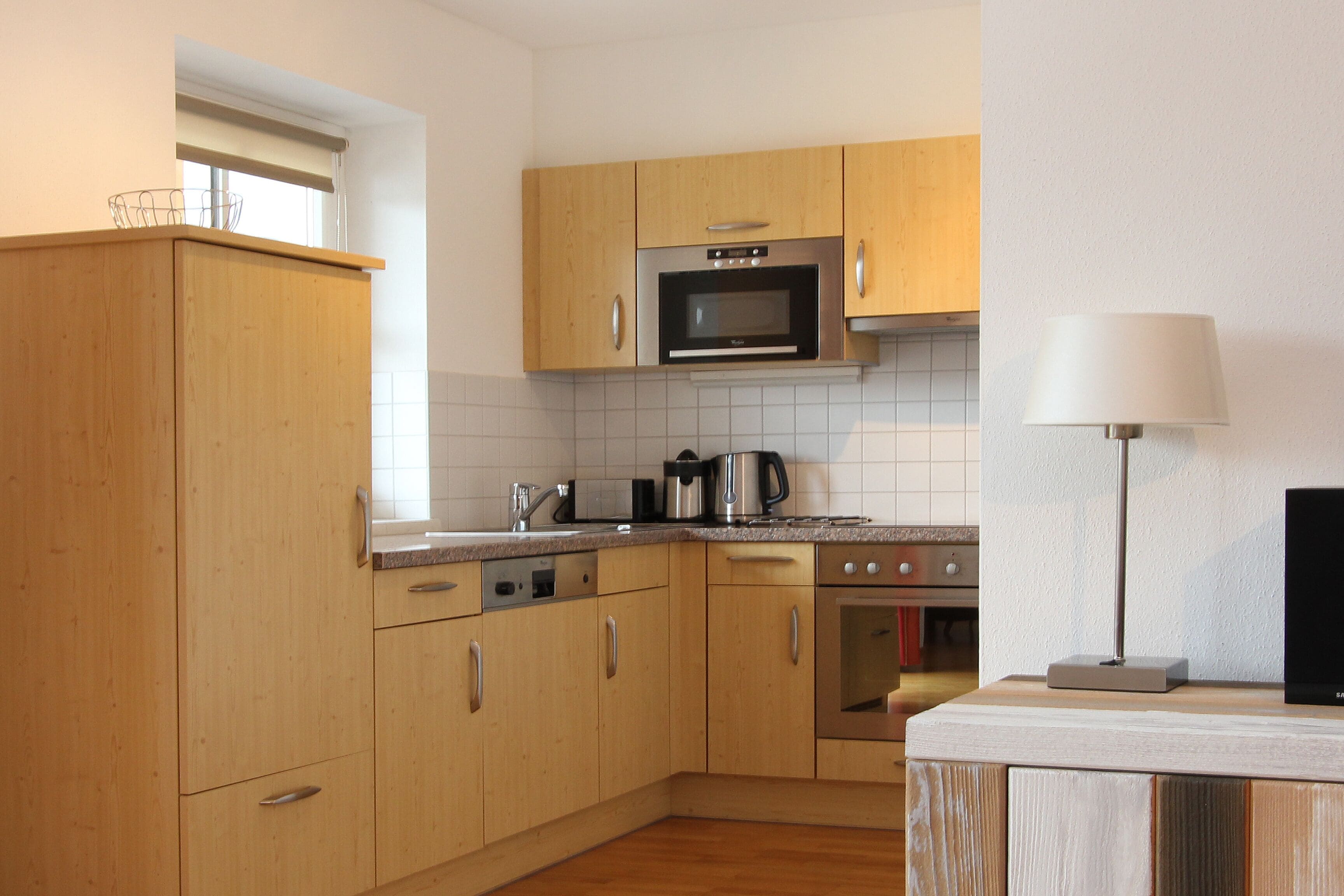 Una cocina moderna con armarios de madera, electrodomésticos de acero inoxidable y un salpicadero de azulejos blancos.