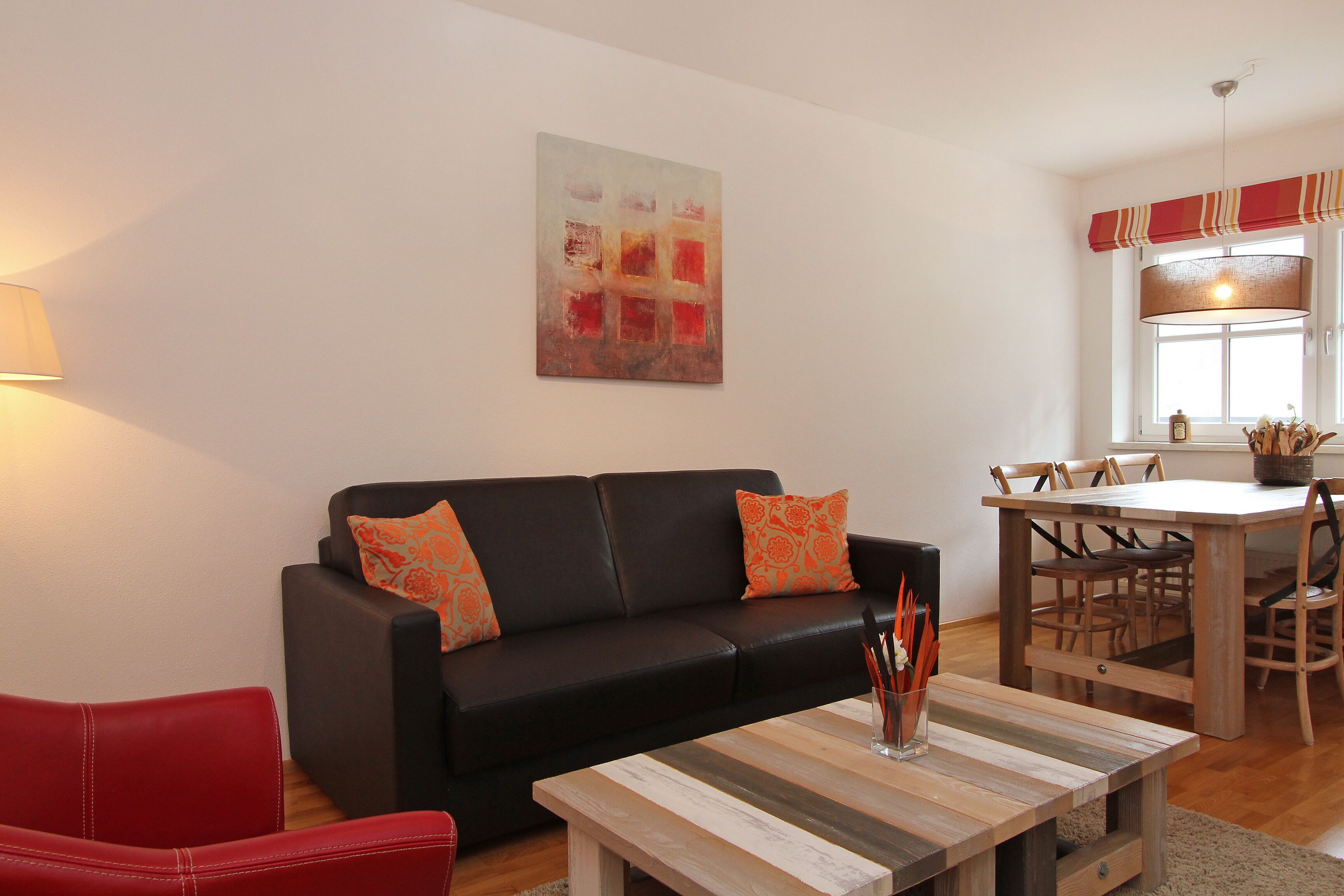 A modern living room with a black leather sofa, a wooden coffee table, and a dining table with chairs.
