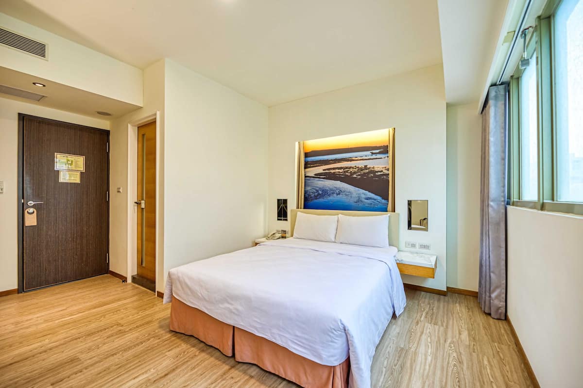 Habitación de hotel con una cama grande, una mesita de noche, teléfono en la pared y ventana con cortinas.