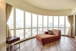 A room with a curved view of a cityscape through large windows, a red sofa with patterned cushions, and a small wooden side table.