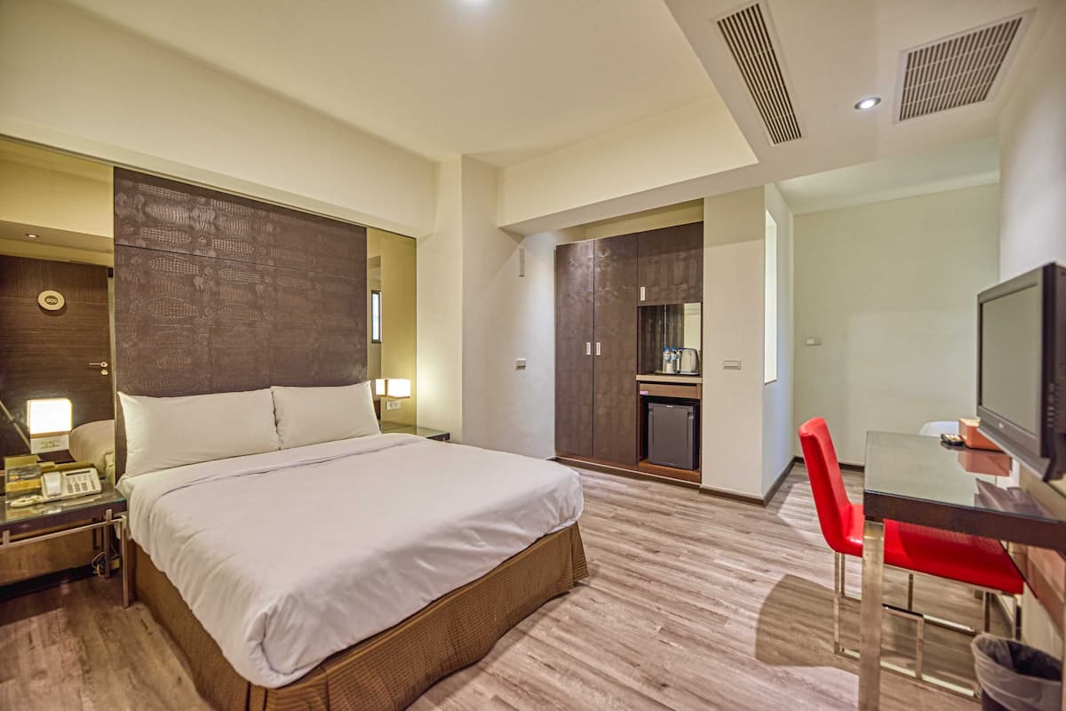 Habitación de hotel con una cama grande, un escritorio con silla, televisión y una kitchenette.