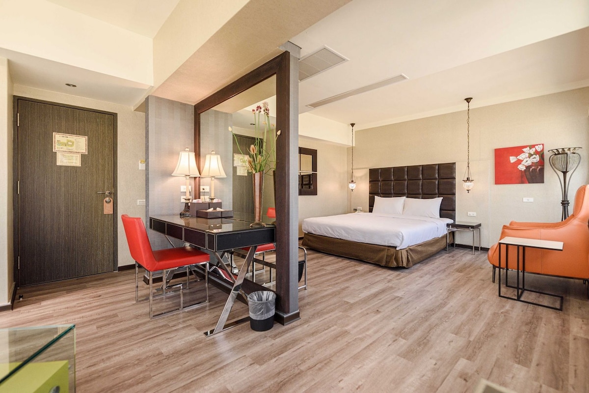 Une chambre d’hôtel comprenant un lit, un bureau avec deux lampes, une chaise, une table de chevet et un miroir.