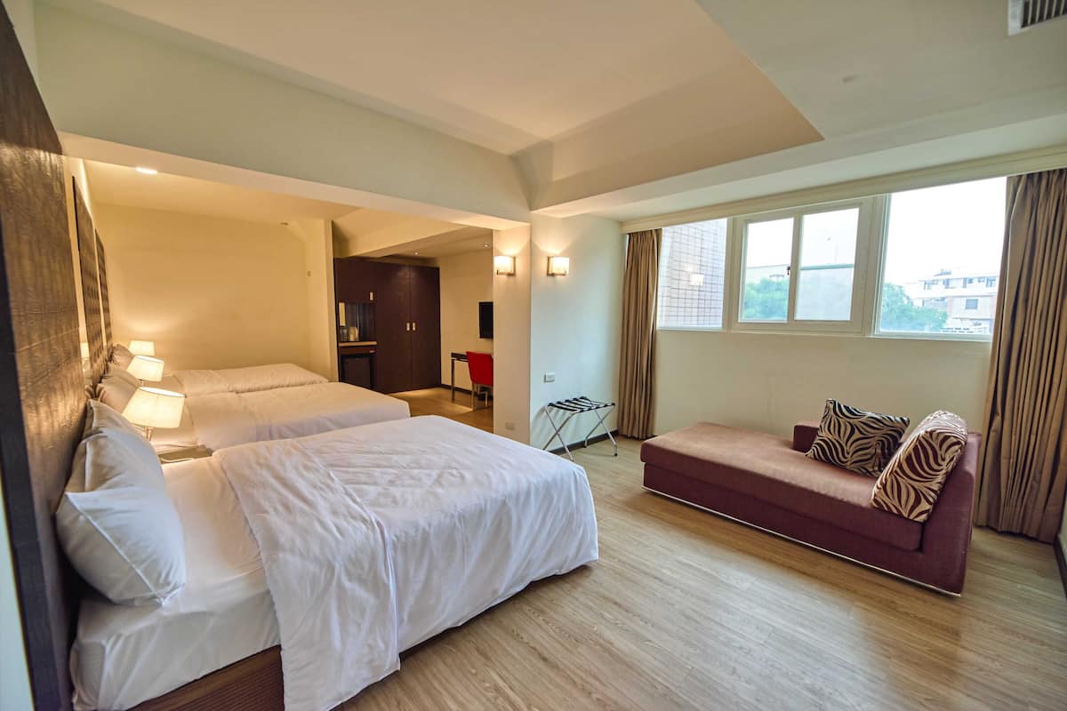 Habitación de hotel con dos camas, un sofá, una ventana con cortinas y una mesita de noche con lámpara.