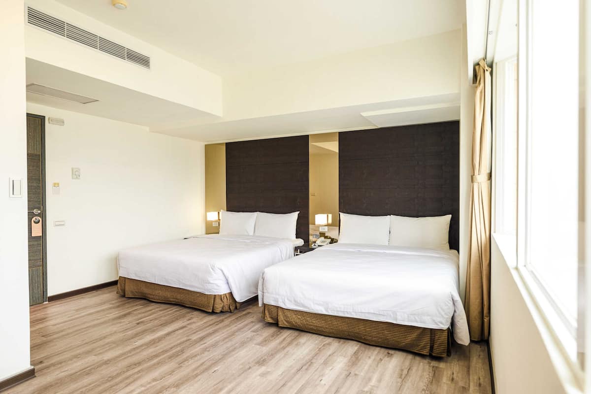 Habitación de hotel con dos camas, suelo de madera y un ventanal con cortinas.