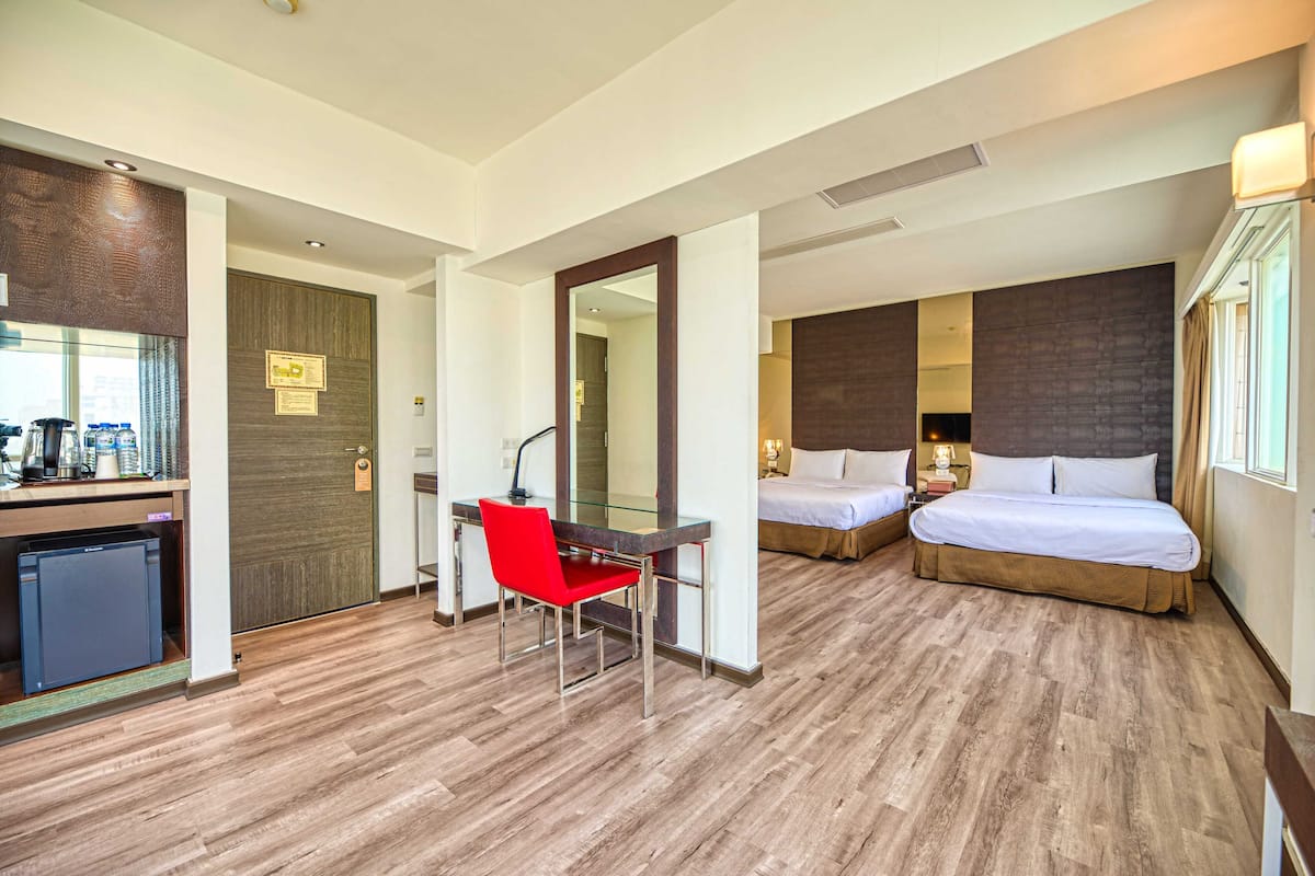 Habitación de hotel con escritorio, una silla roja, dos camas, un espejo y una pequeña cocina.