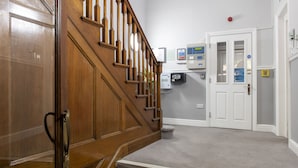 A wooden staircase leading to a landing with a white door and a control panel on the wall. - SACO Bristol- West India House (Bristol)
