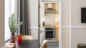 A modern dining area with a table and chairs, a potted plant, and a view into a kitchen with a stove and oven. - SACO Bristol- West India House (Bristol)