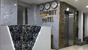 A modern airport hotel reception area with marble walls, a reception desk, and clocks on the wall.