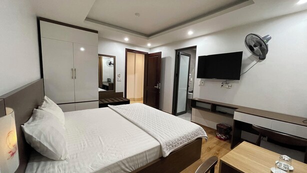 A hotel room with a bed, a desk, a chair, a TV, and a wardrobe.