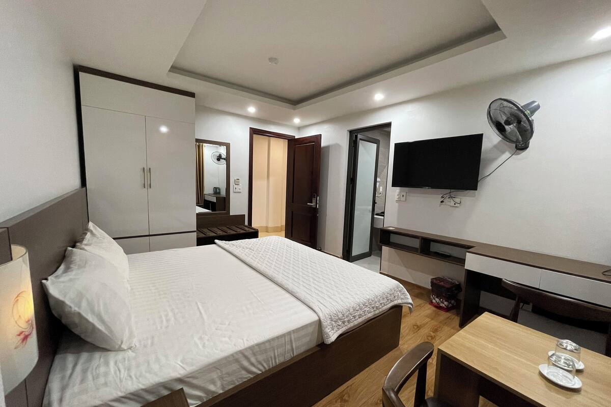 A hotel room with a bed, a desk, a chair, a TV, and a wardrobe.