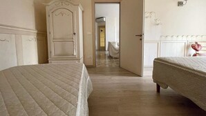 A hotel room with two beds, a wardrobe, and a door leading to another room. - Casa Camilla City (Padova)