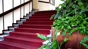 A staircase with red carpeted steps and a wooden handrail, surrounded by lush green plants. - Casa Camilla City (Padova)