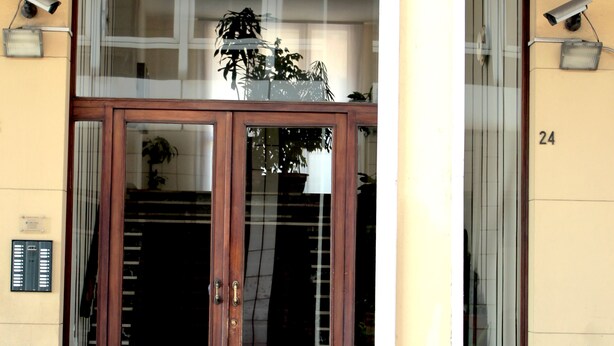 A building entrance with a glass door, a potted plant, and a security camera. - Casa Camilla City (Padova)