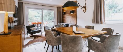 A modern dining area with a wooden table and grey upholstered chairs, a large pendant light, and a view of the outdoors through a sliding glass door.