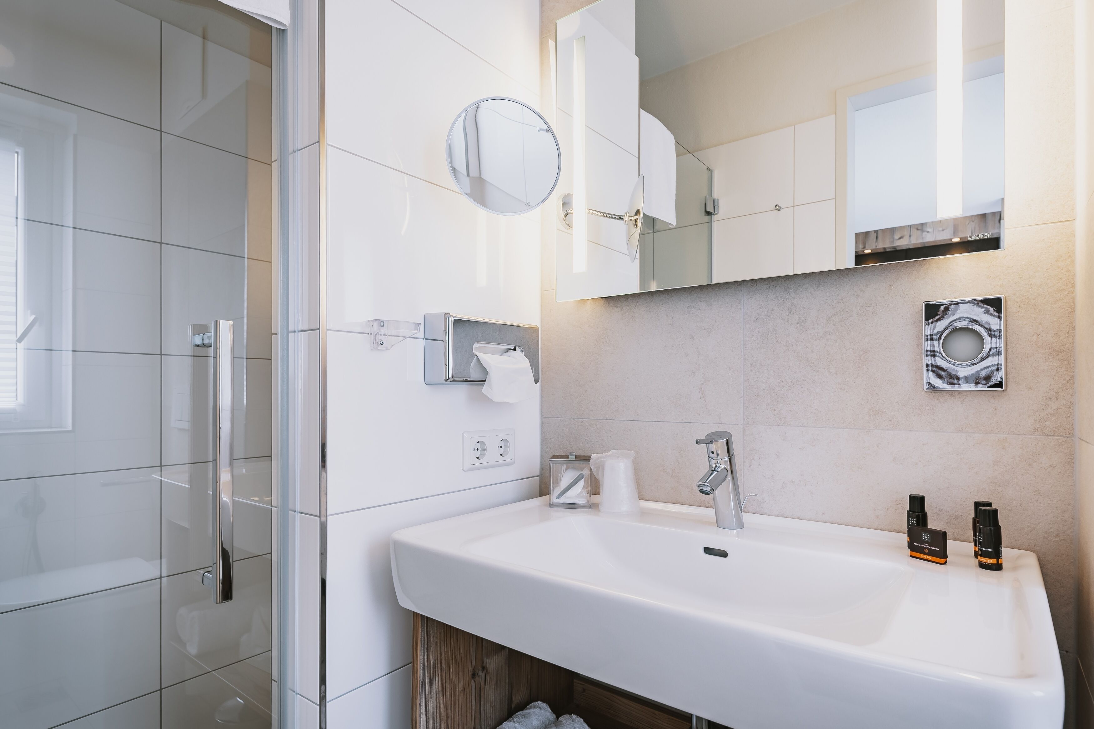 A modern bathroom with a large sink, a mirror, and a shower area.