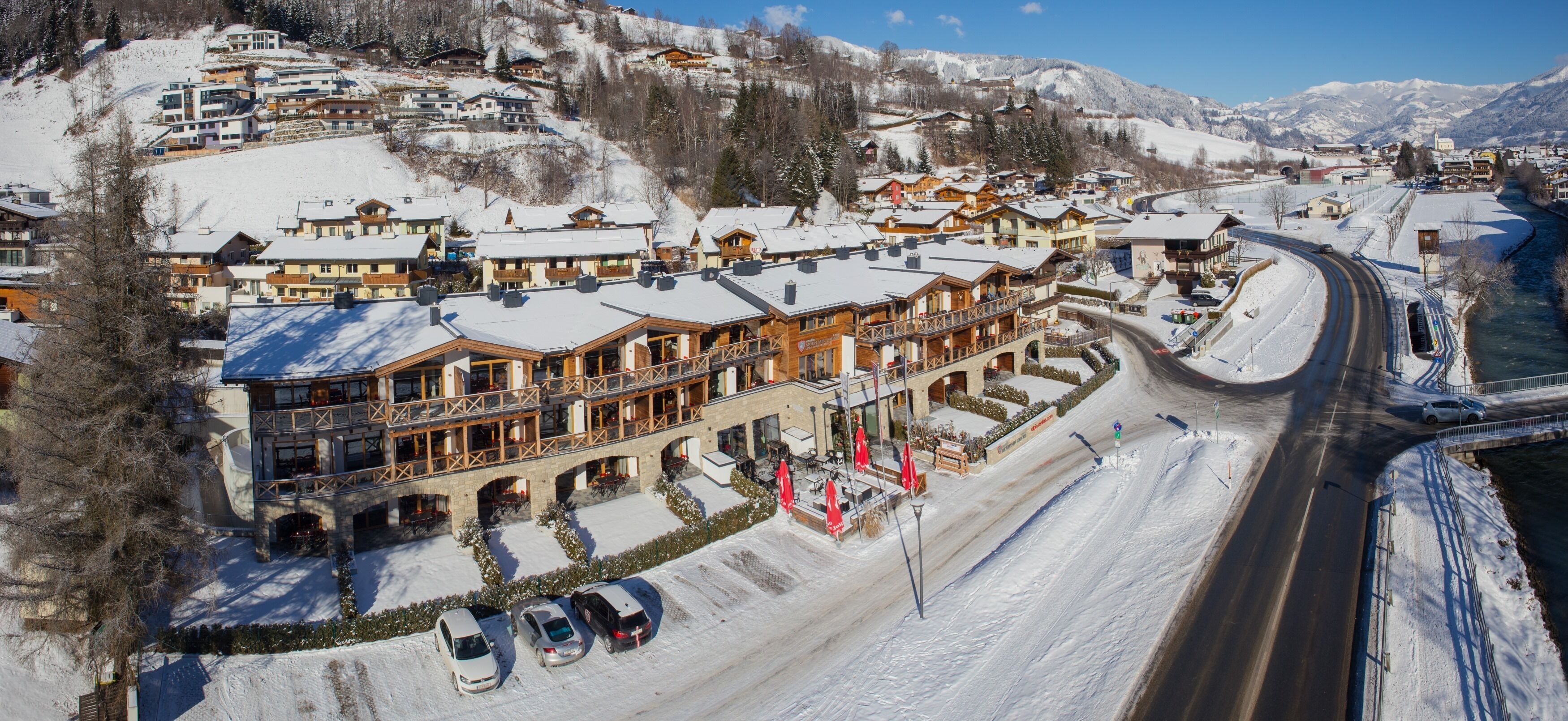 A hotel with multiple balconies, a ski slope in the background, and a parking area.