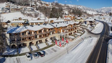 Un hôtel doté de nombreux balcons, avec une piste de ski en arrière-plan et un espace de stationnement.