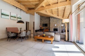 Ampla sala de estar com teto de madeira, lareira de pedra e mobiliário moderno.