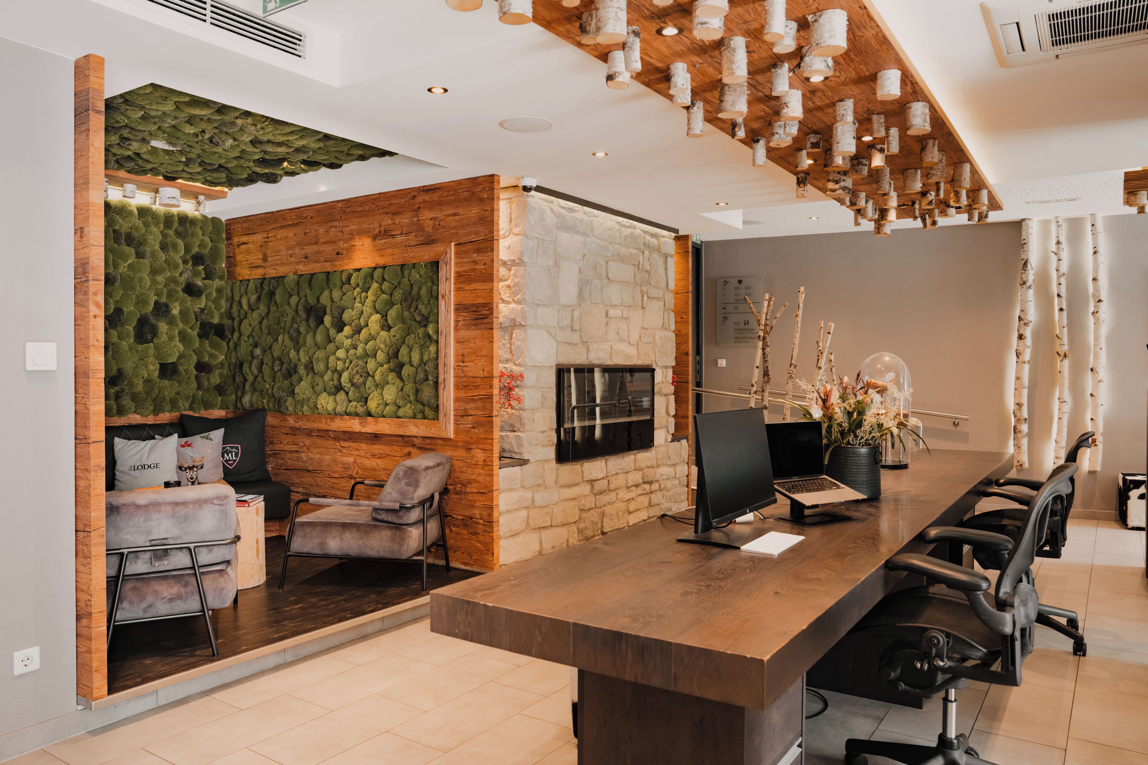 A modern reception area with a stone wall, green wall, and a fireplace. There are sofas and chairs for guests.